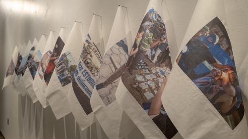 Images printed on white cloths, hanging in a line on a white wall.