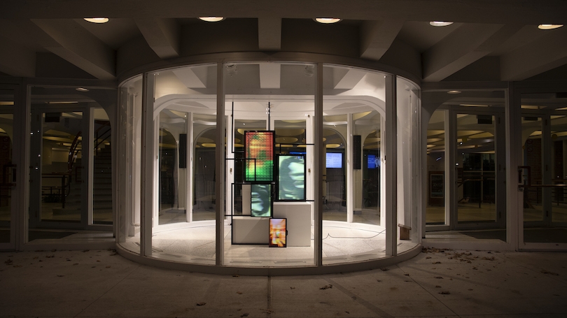 Image shows the Barrows Rotunda, a circular glass building with four screens showing different pixelated or blurred images in different colors rangind from orange to green-gray and five other empty frames.