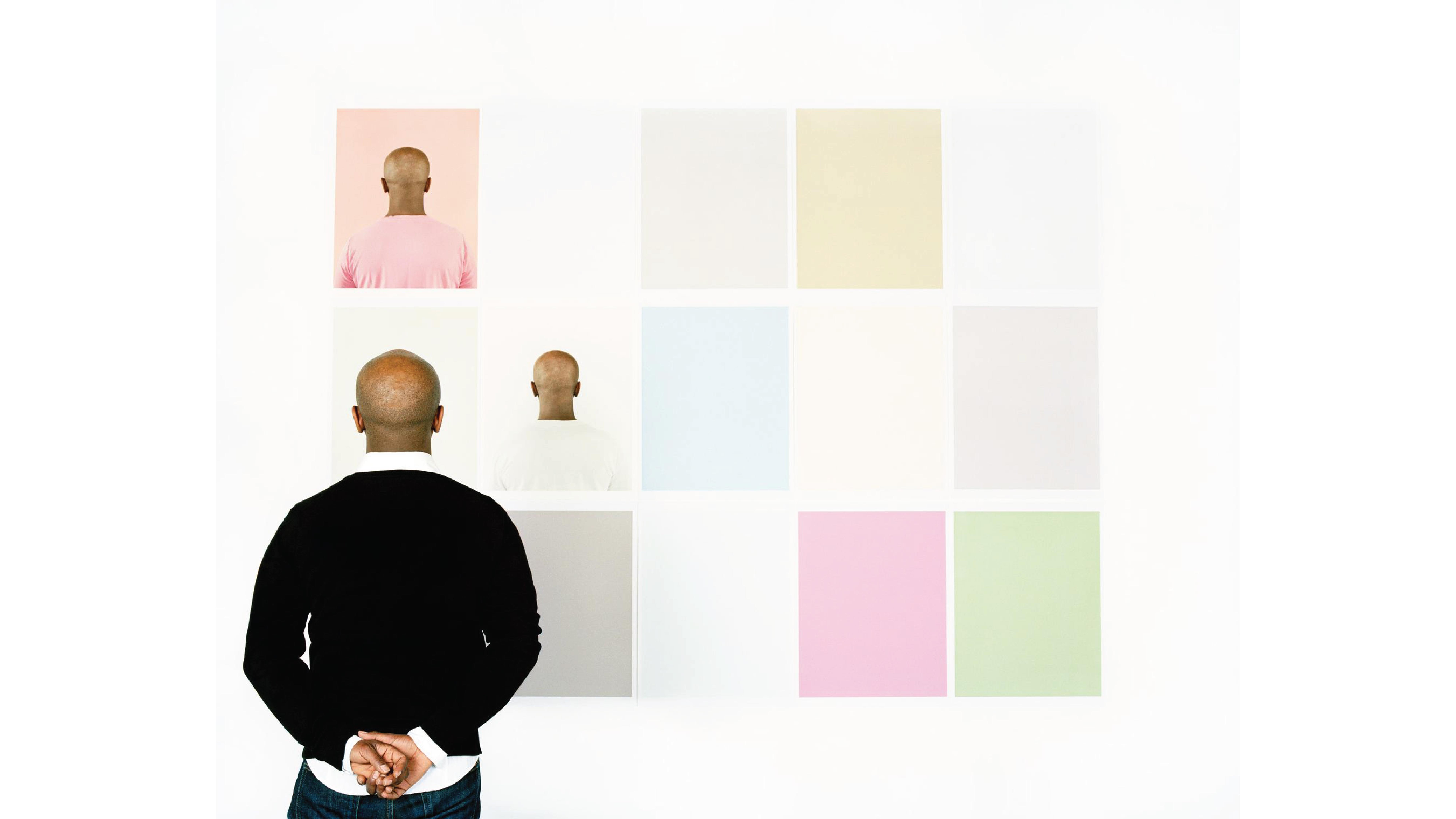 A man facing away from the camera looking at portraits on a wall